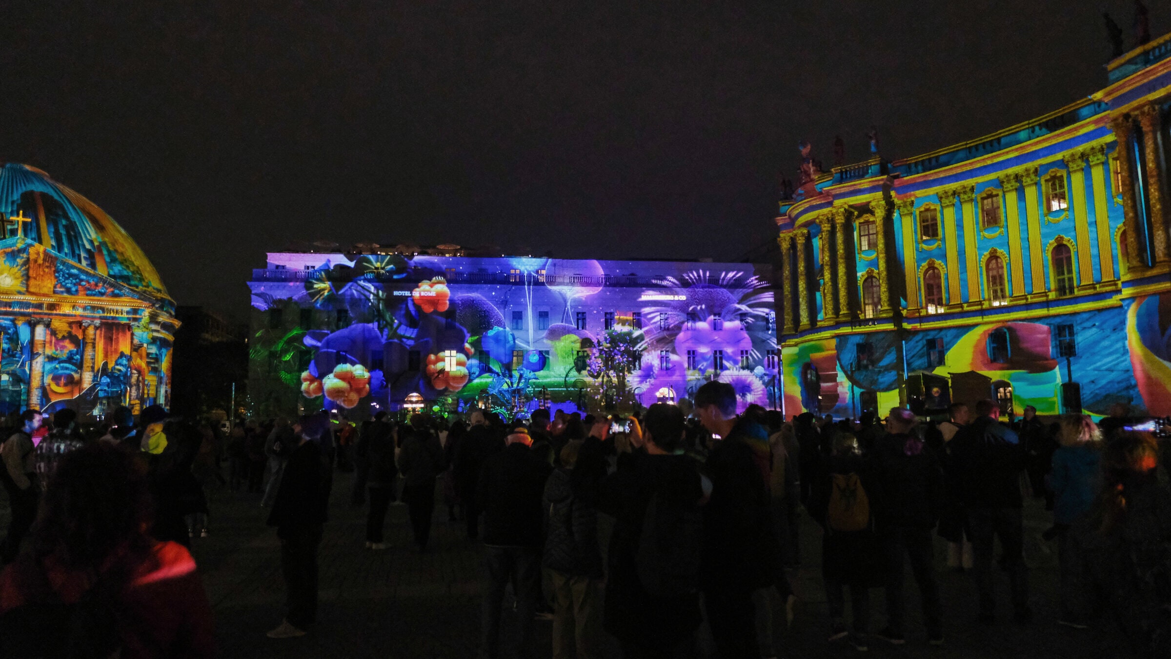 Bebelplatz during the Festival of Lights, facades lit with projected artwork, crowds watching.