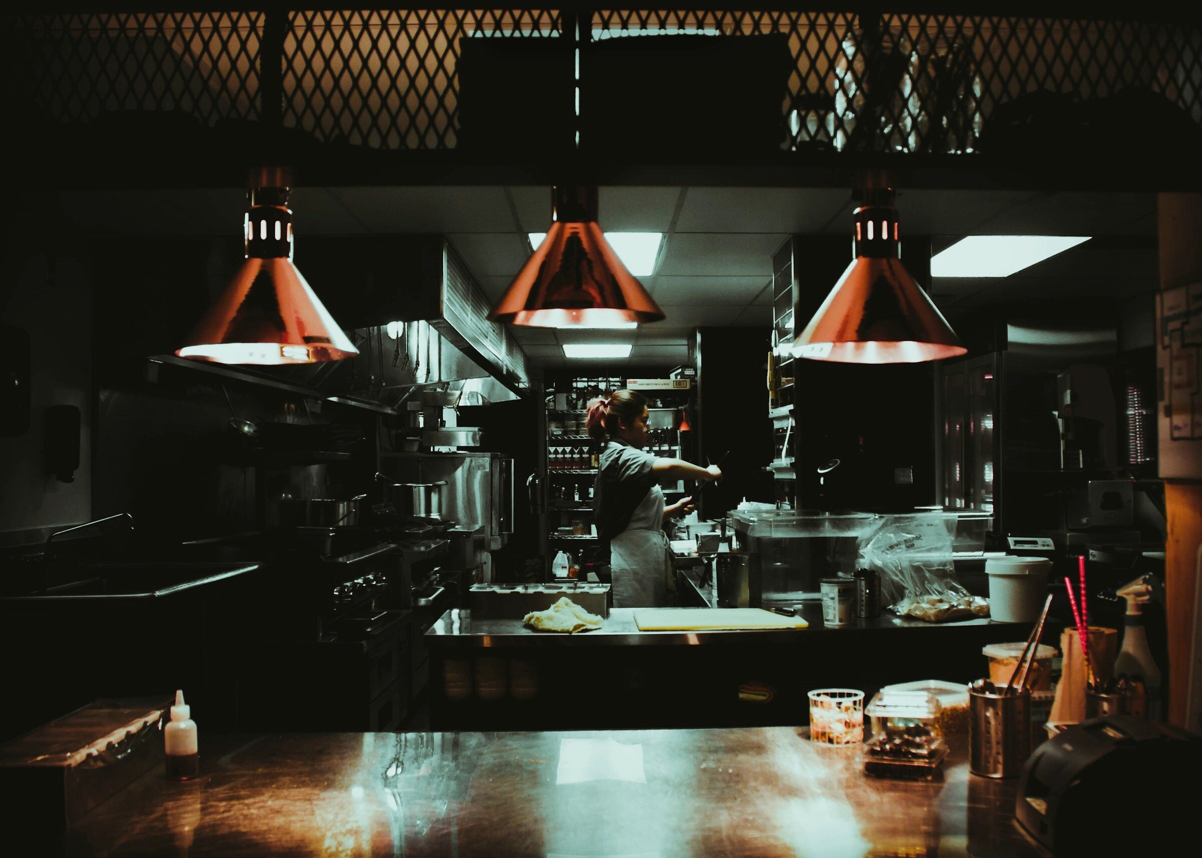 A kitchen under red pendant lamps, steel counters, quiet.