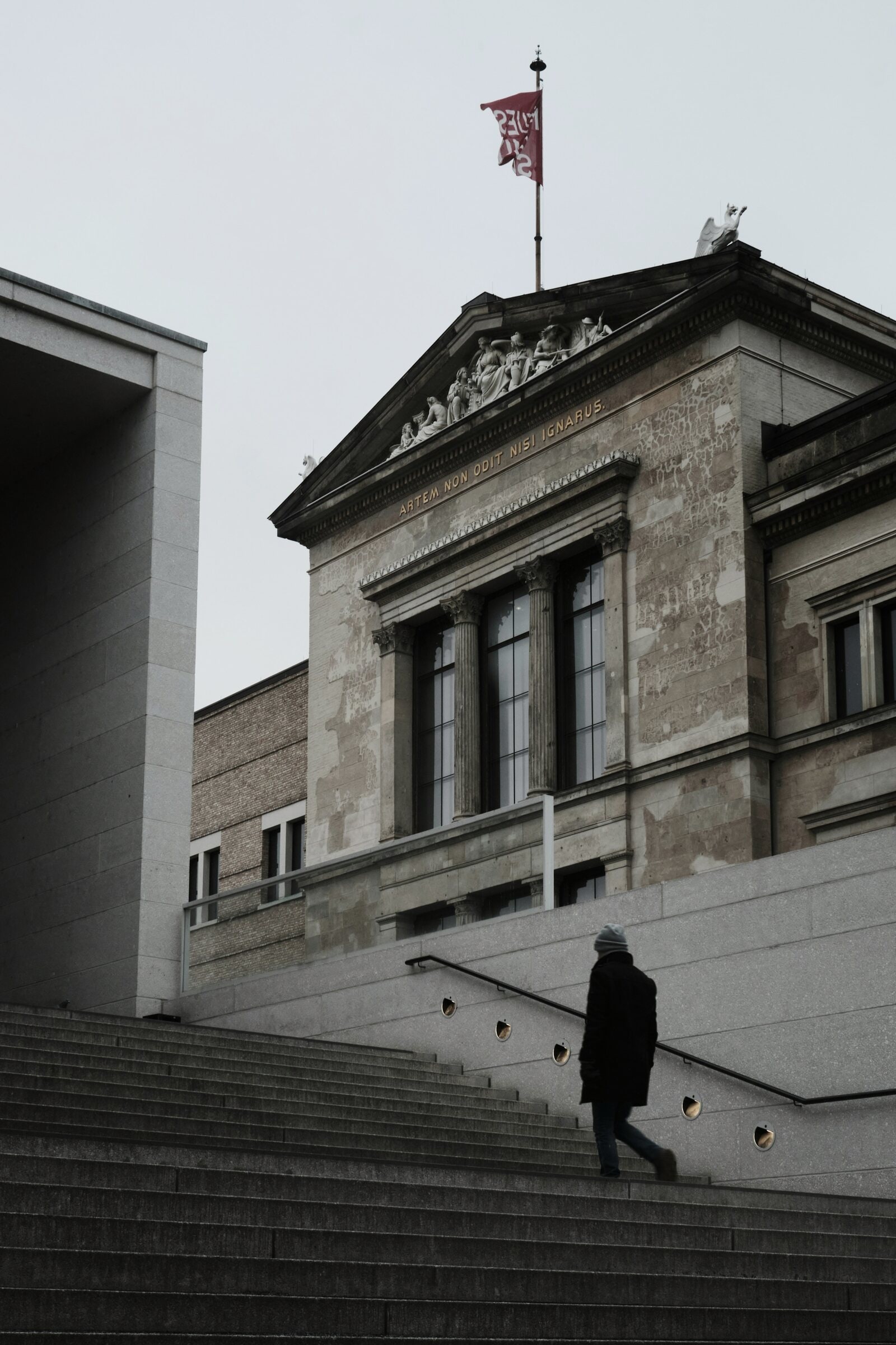 A single figure climbing the stone steps of the Neues Museum.