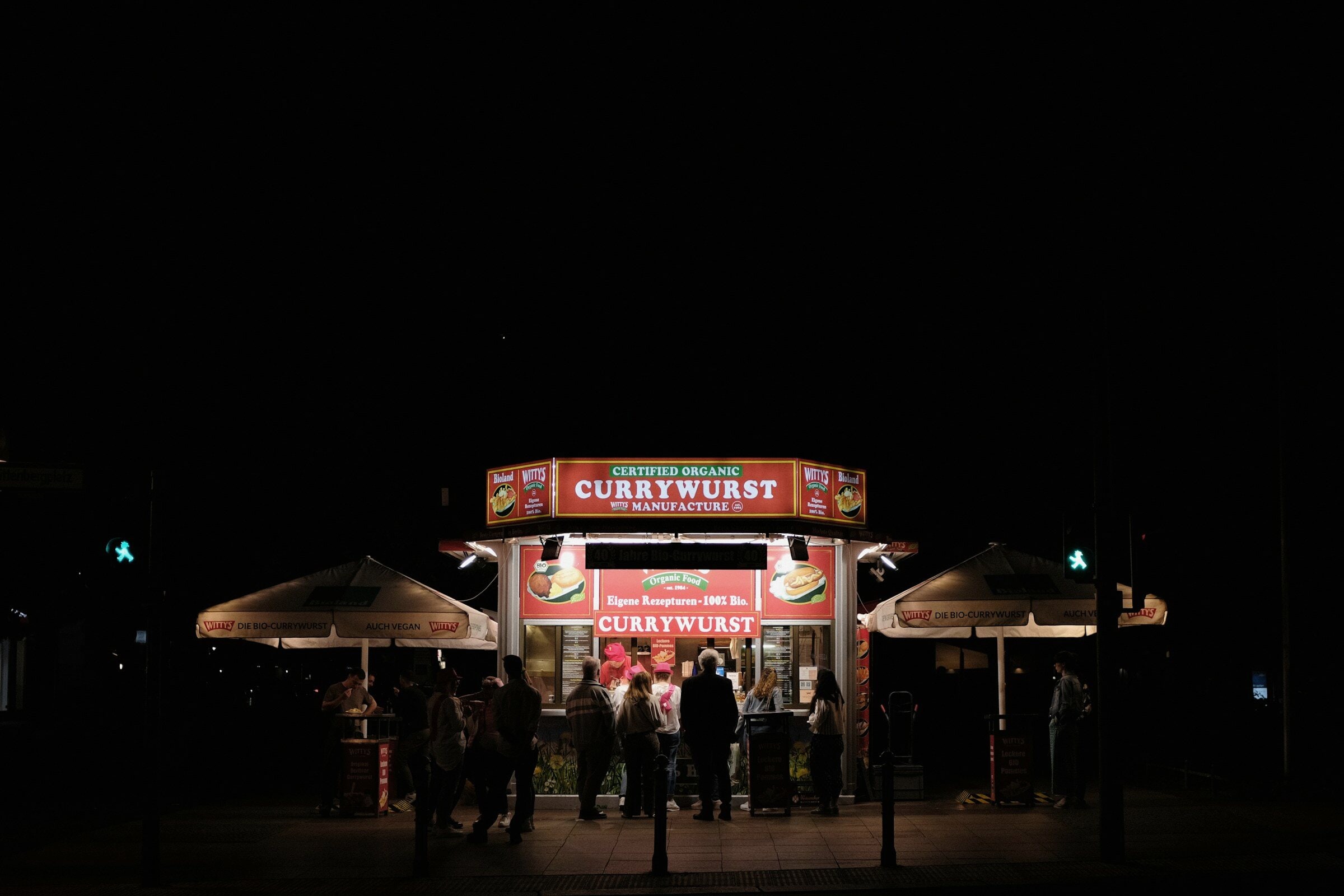 A currywurst stand lit at night with a small crowd.