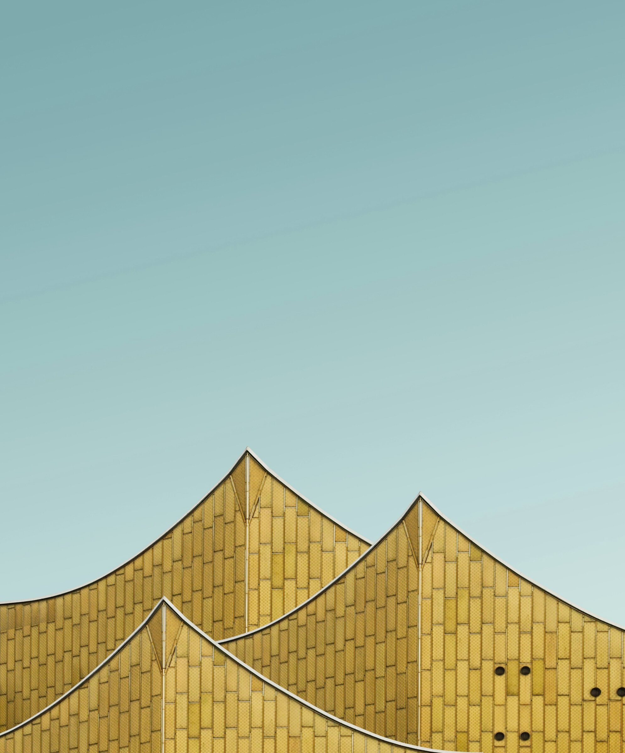 The gold-clad facade of the Berlin Philharmonie against a clear sky.